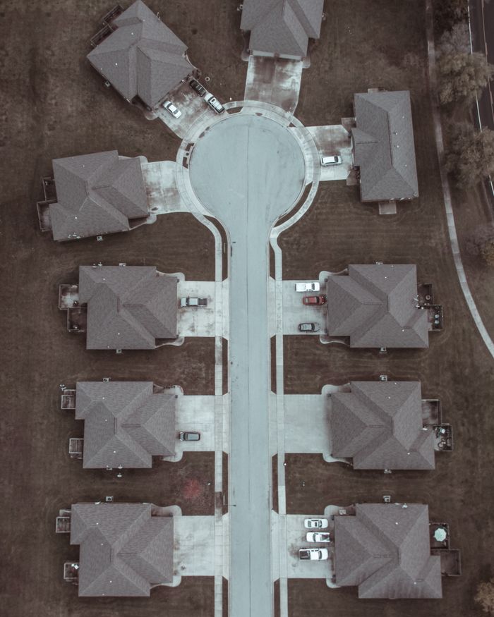 Aerial shot of a suburban cul-de-sac with identical houses and parked cars.