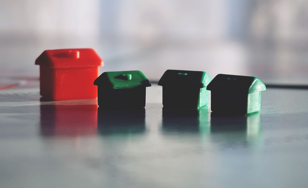 Services Close-up photo of red and green Monopoly game houses on a reflective surface.
