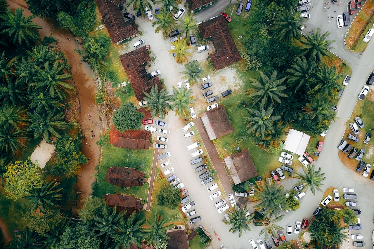 Drone view of automobiles parked near accommodation houses surrounded by green palms in tropical country