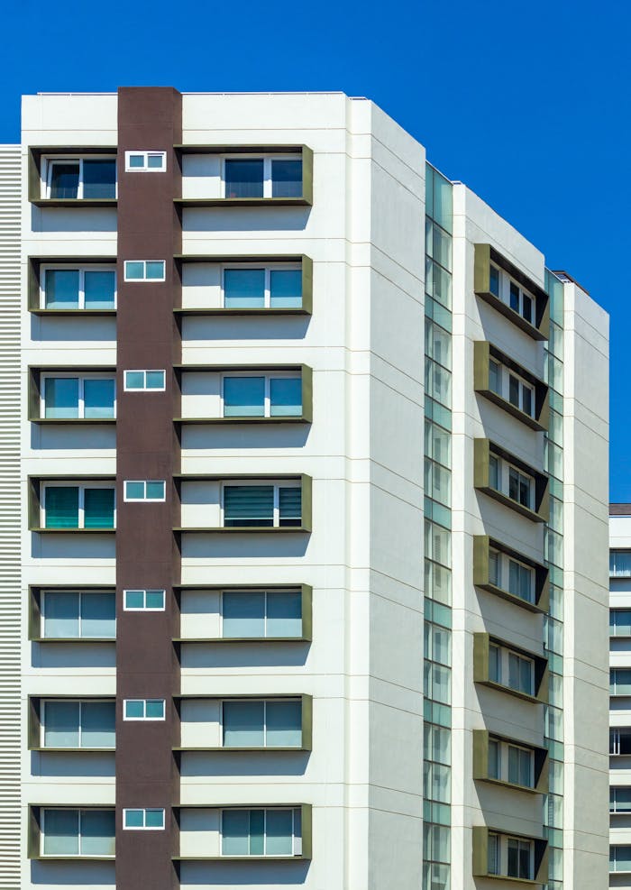 Exterior of residential multistory house with white walls with windows located against blue sky in sunlight in daytime in street